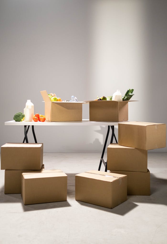 contact-img Cardboard boxes filled with assorted groceries on a white folding table indoors.